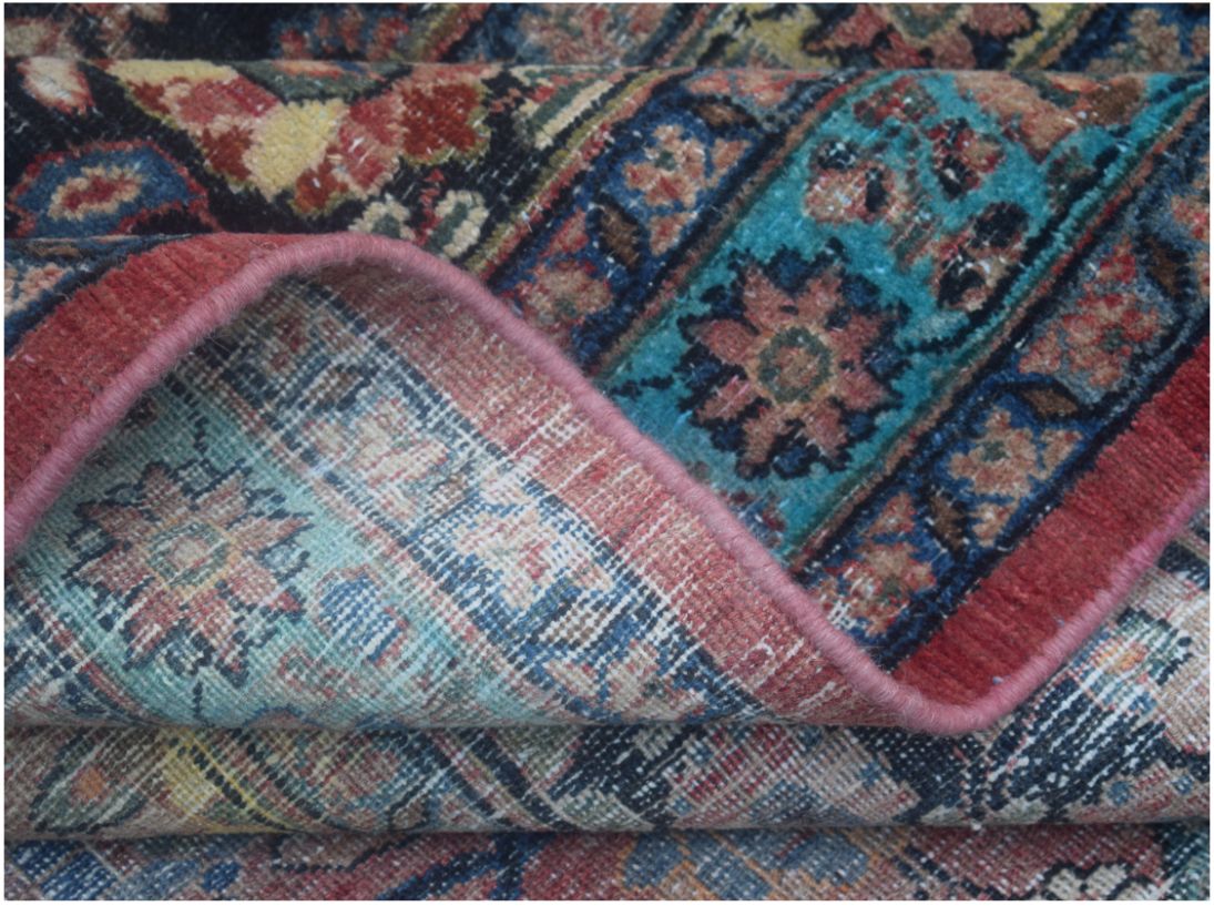 A folded corner of a vintage Persian wool rug featuring intricate floral patterns in vibrant colors.