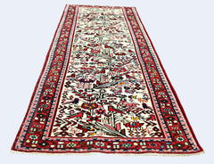 A vintage Persian runner rug featuring a cream field with intricate red and multi-colored motifs.