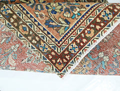 A vintage Persian runner with a folded corner revealing intricate floral patterns in wool.