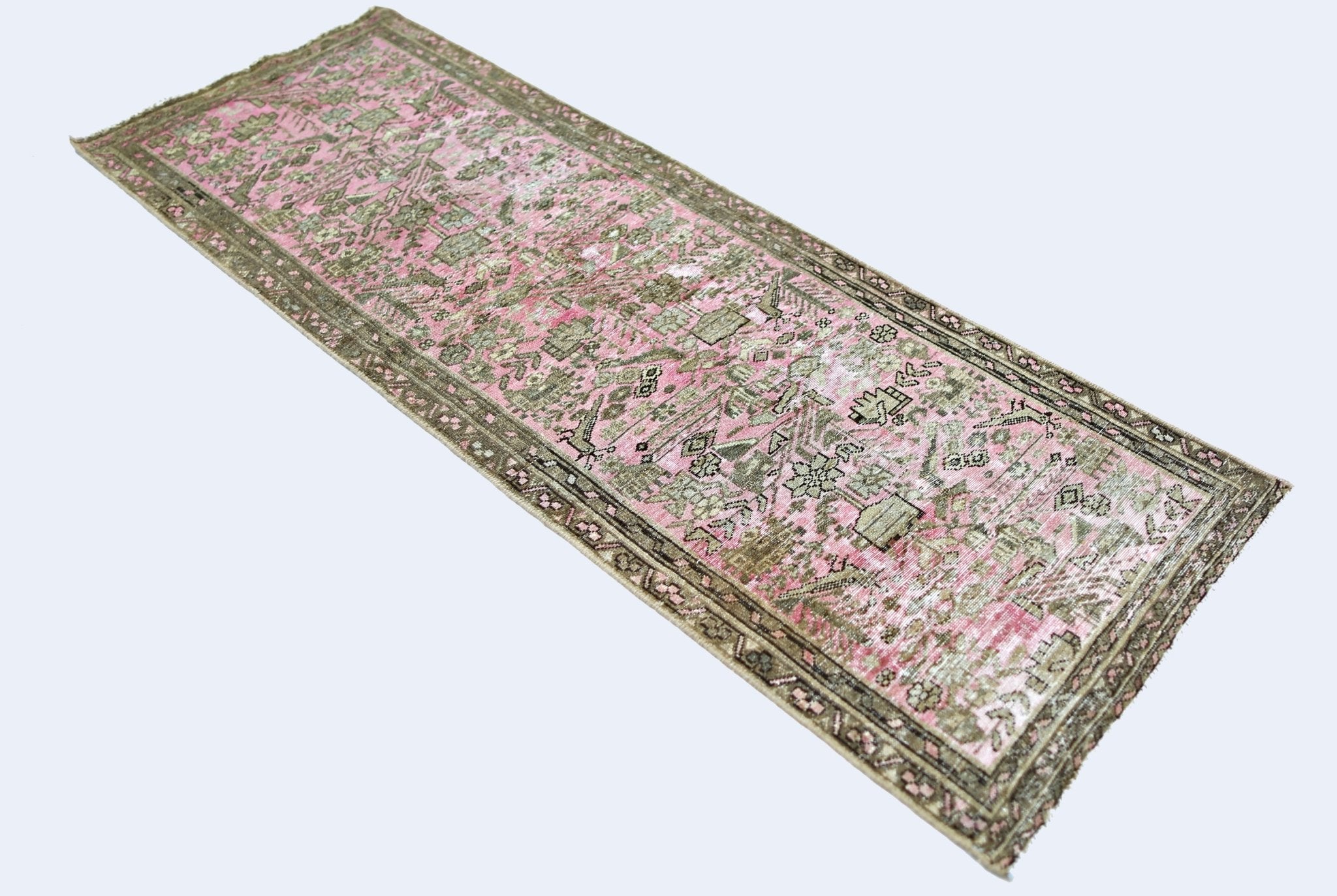 A vintage Persian runner rug featuring a faded pink and green floral pattern on a white background.