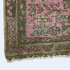 A close-up of a vintage Persian runner featuring a pink field with intricate brown floral patterns.