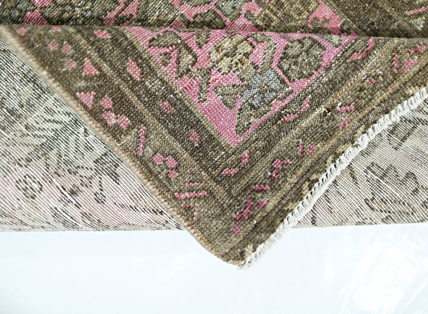 A folded vintage Persian runner featuring a traditional floral pattern in pink and brown tones.