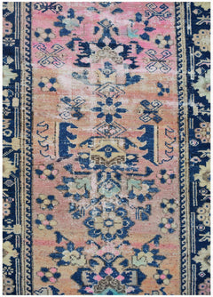 A vintage Persian runner featuring a faded pink and orange field with intricate blue floral motifs.