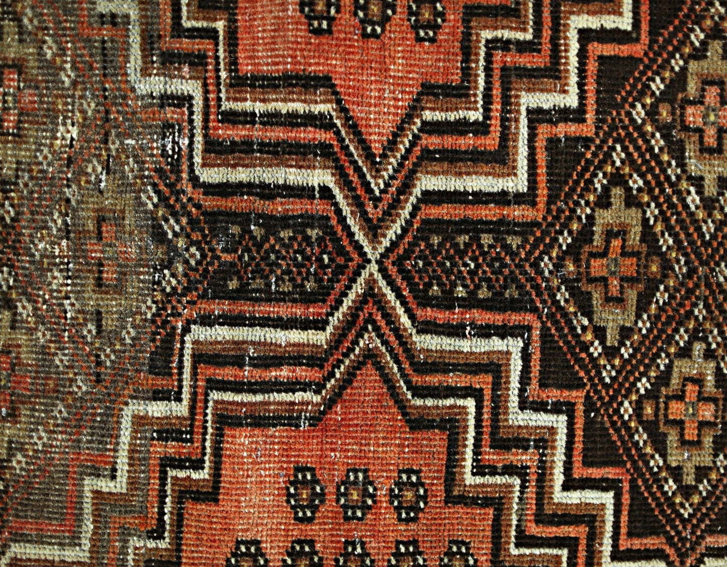 A close-up of a vintage Persian runner featuring geometric patterns in red, brown, and cream.
