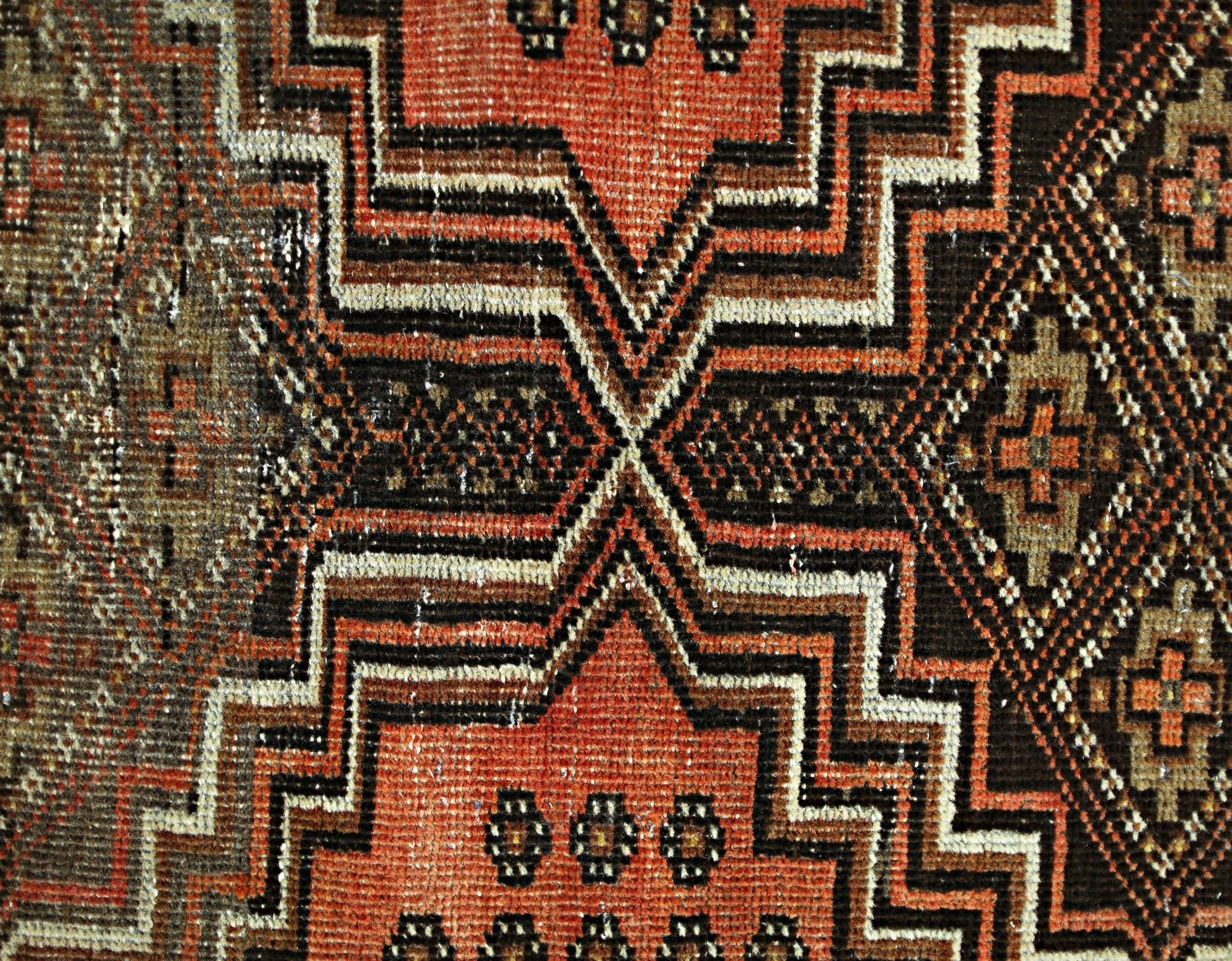 A close-up of a vintage Persian runner featuring geometric patterns in red, brown, and cream.