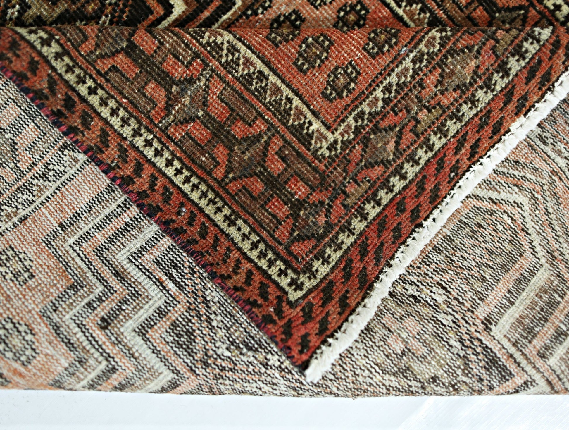 A folded vintage Persian runner featuring intricate geometric patterns in red and brown wool.