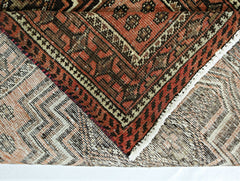 A folded vintage Persian runner featuring intricate geometric patterns in red and brown wool.