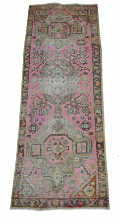 A vintage Persian runner rug featuring a pink field with intricate geometric and floral patterns.
