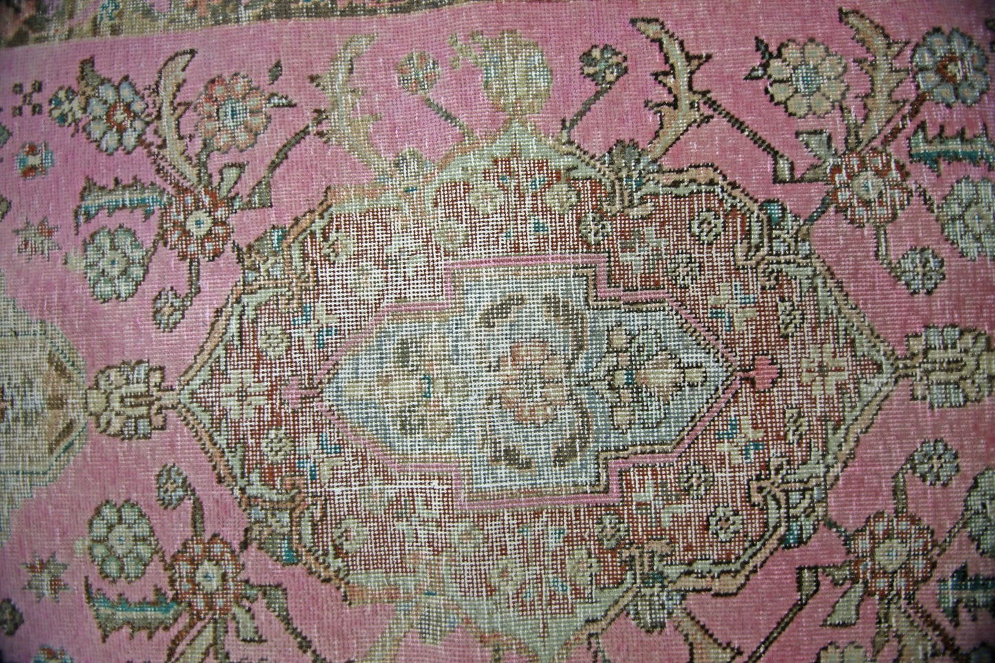 A vintage Persian runner featuring a central floral medallion on a faded pink wool background.