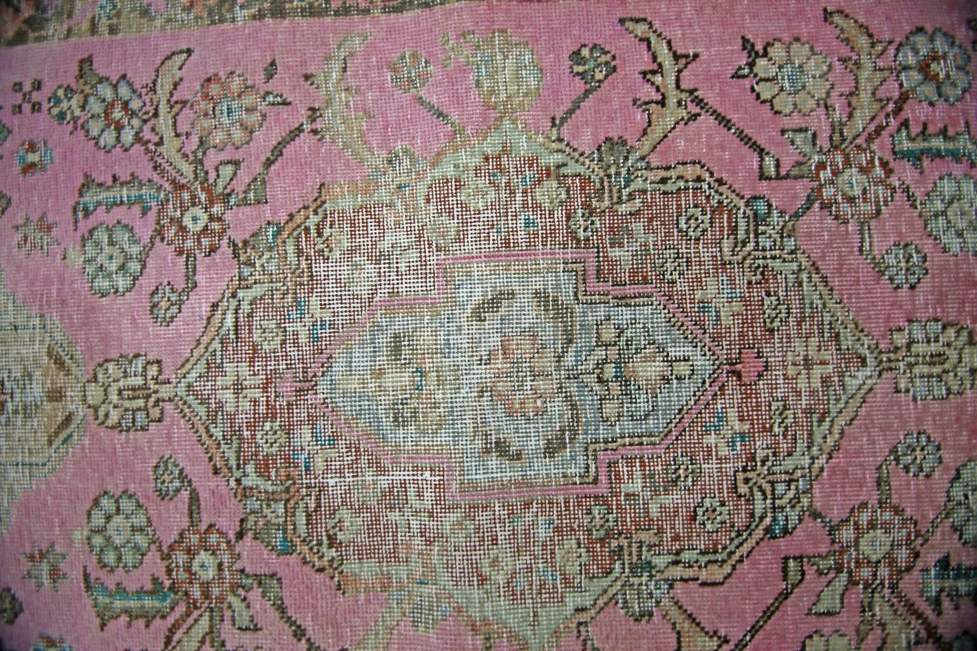 A vintage Persian runner featuring a central floral medallion on a faded pink wool background.