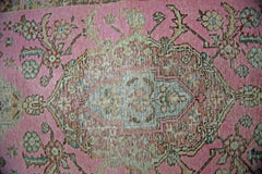 A vintage Persian runner featuring a central floral medallion on a faded pink wool background.