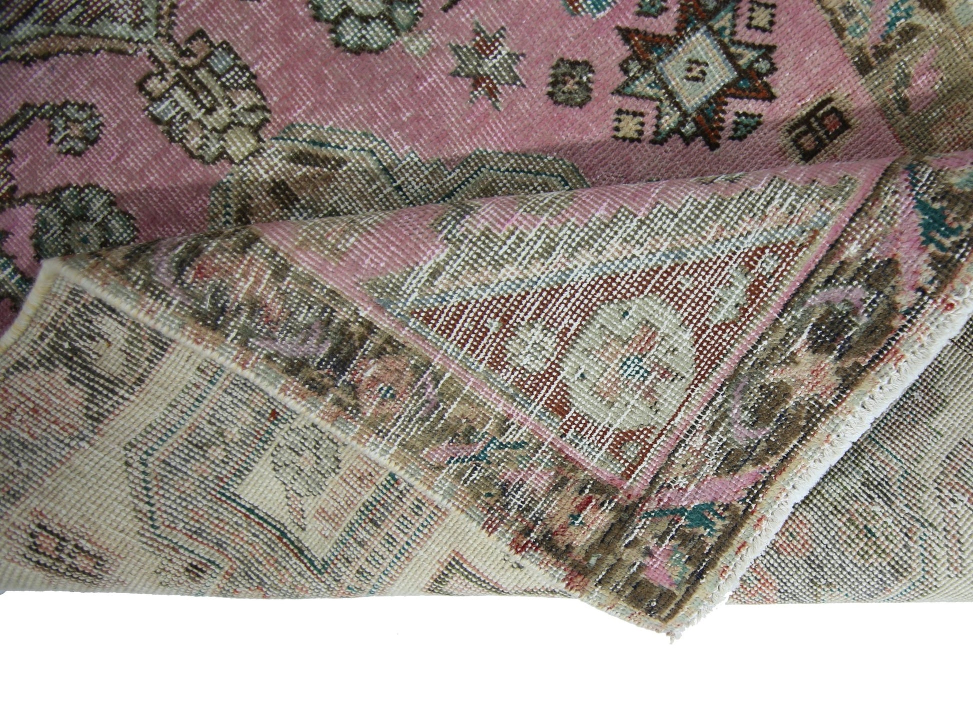 A folded vintage Persian runner featuring a pink field with intricate geometric and floral patterns.