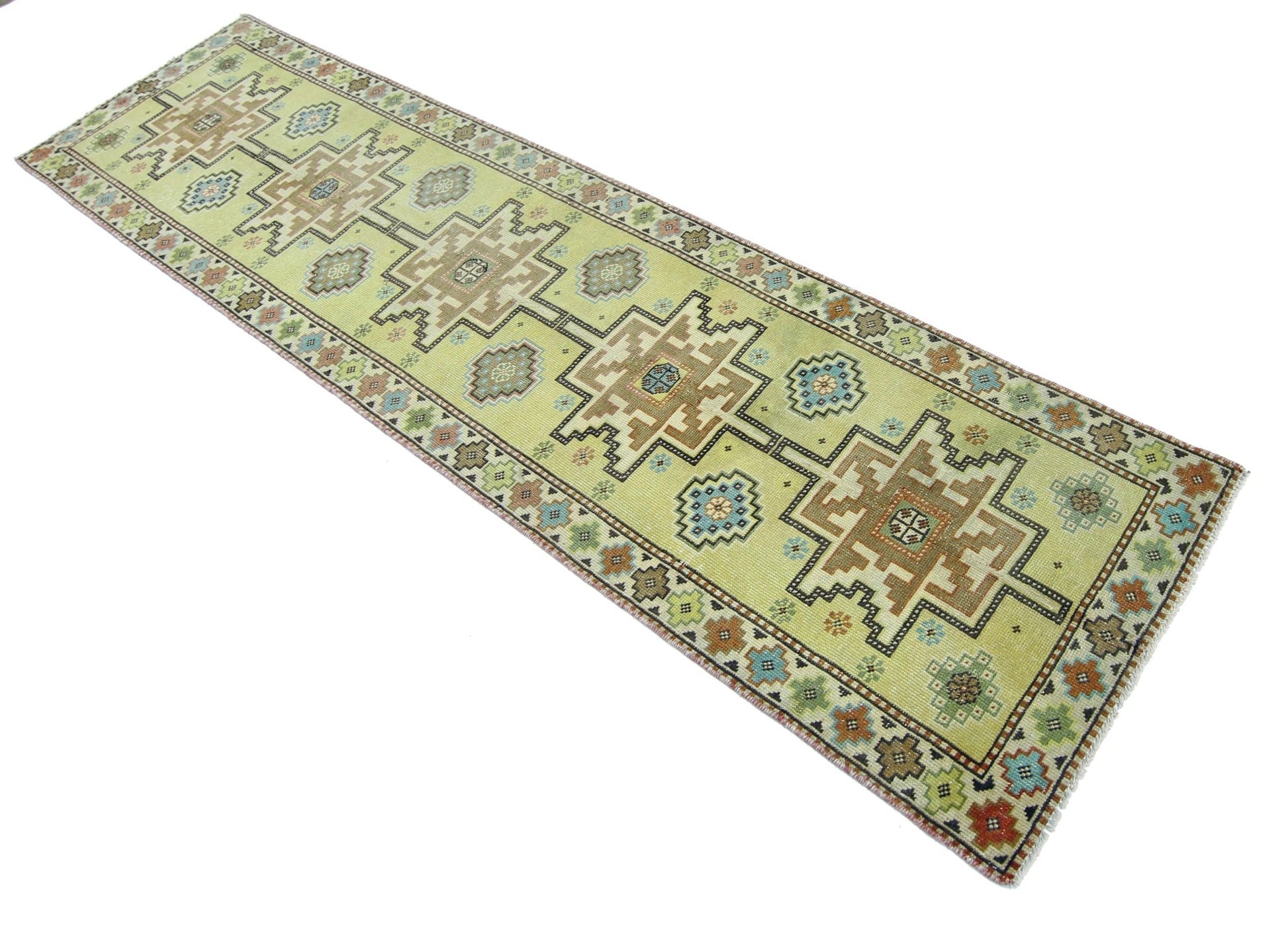 A handmade vintage Persian runner rug featuring geometric patterns in muted tones on a yellow field.
