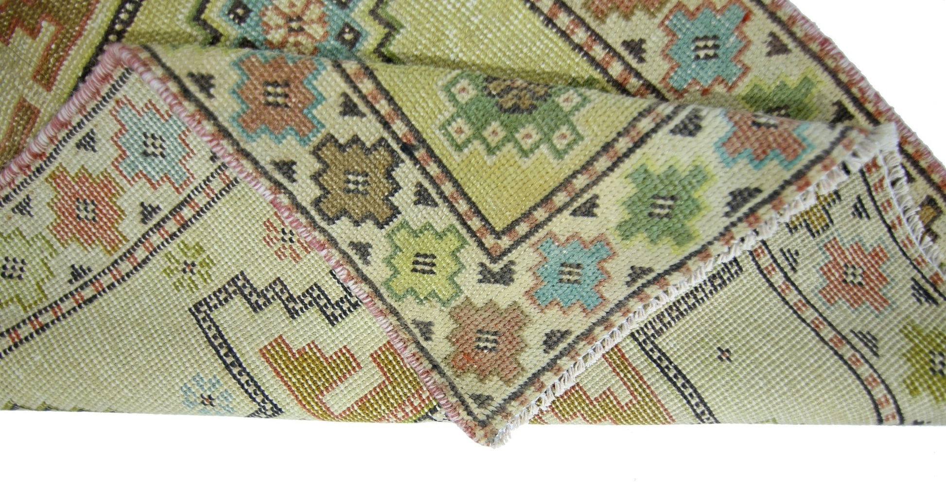 A folded vintage Persian runner featuring geometric patterns in muted green, blue, and brown tones.