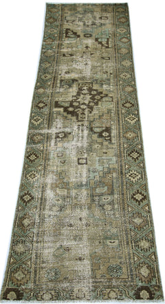 A vintage handmade Persian runner rug featuring a distressed geometric pattern in muted earth tones.