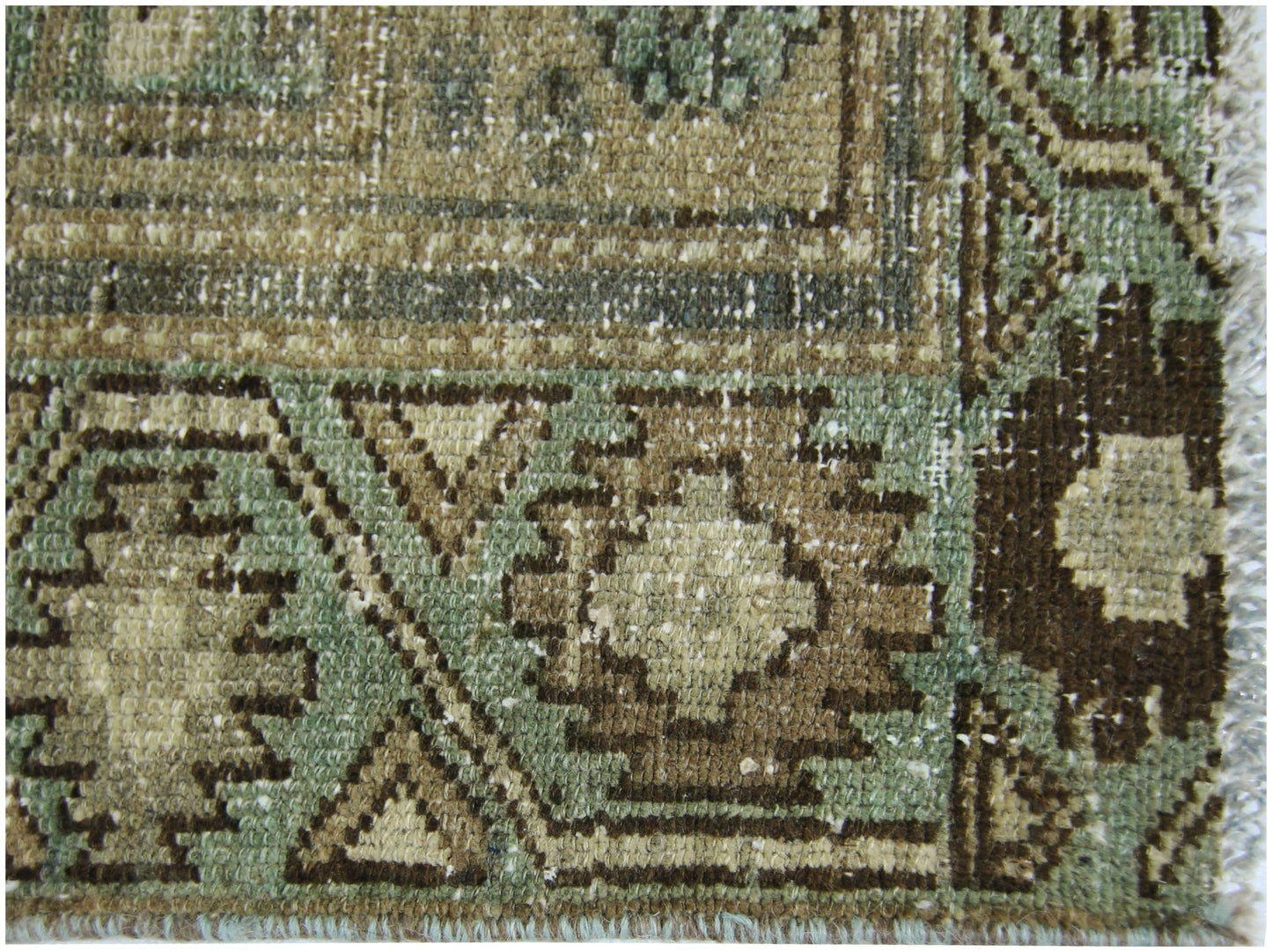 A close-up of a vintage Persian runner featuring geometric patterns in shades of green and brown.