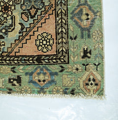 A vintage Persian runner featuring a geometric pattern in shades of green, peach, and blue.