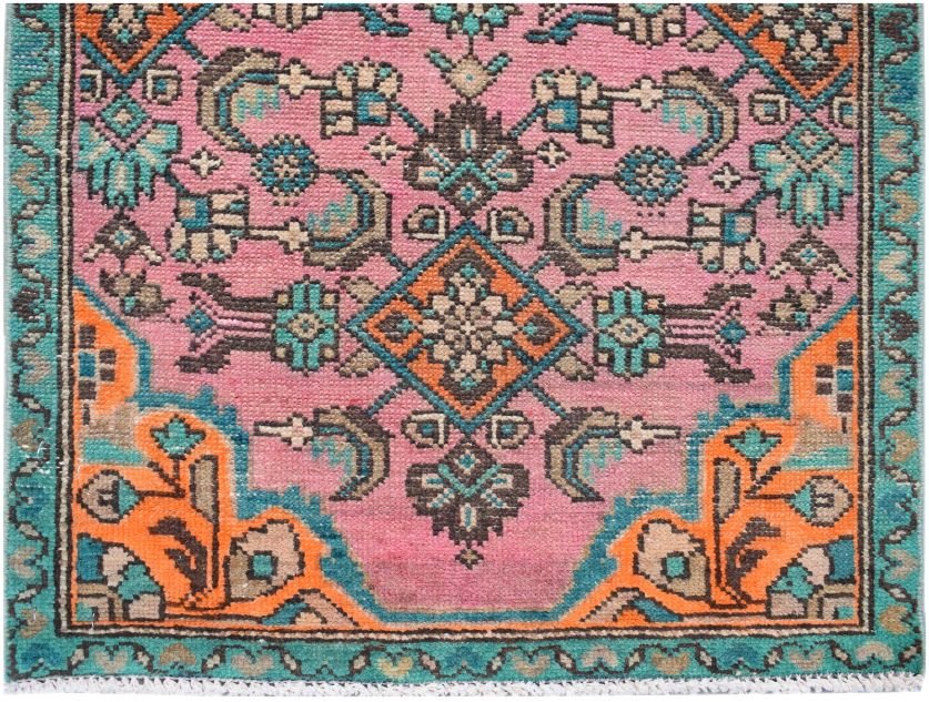 A vintage Persian runner featuring a pink field with geometric floral patterns in orange and teal.