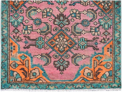 A vintage Persian runner featuring a pink field with geometric floral patterns in orange and teal.