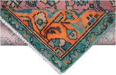 A corner of a vintage Persian runner featuring a vibrant orange, teal, and pink geometric pattern.
