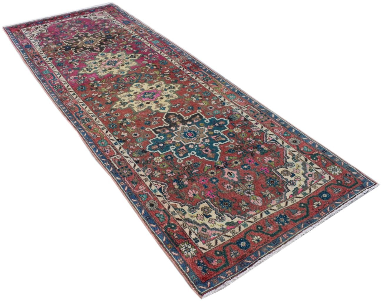 A vintage Persian runner rug featuring intricate floral patterns in red, blue, and cream tones.