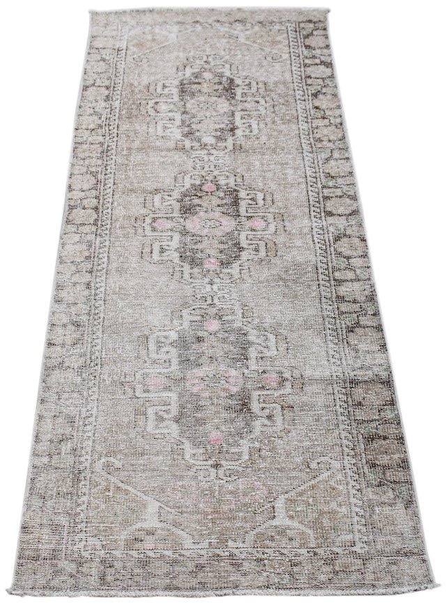 A vintage Persian runner rug featuring a faded beige pattern with brown and soft pink accents.