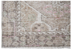 A vintage Persian runner rug featuring a faded geometric pattern in neutral tones with pink accents.