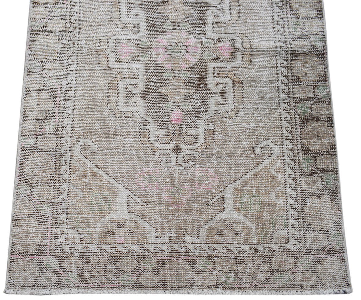A handwoven vintage Persian runner featuring a faded geometric pattern in beige and soft pink.