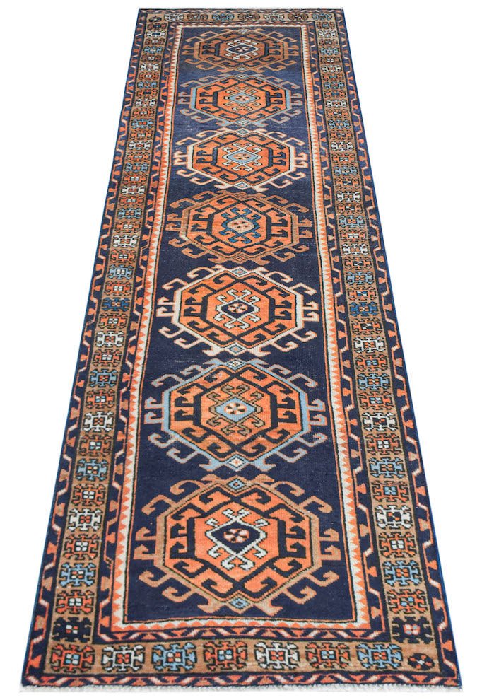A handwoven vintage Persian runner featuring repeating orange octagonal motifs on a navy blue field.