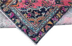 A corner of a vintage Persian runner featuring a vibrant pink field and a dark blue floral border.