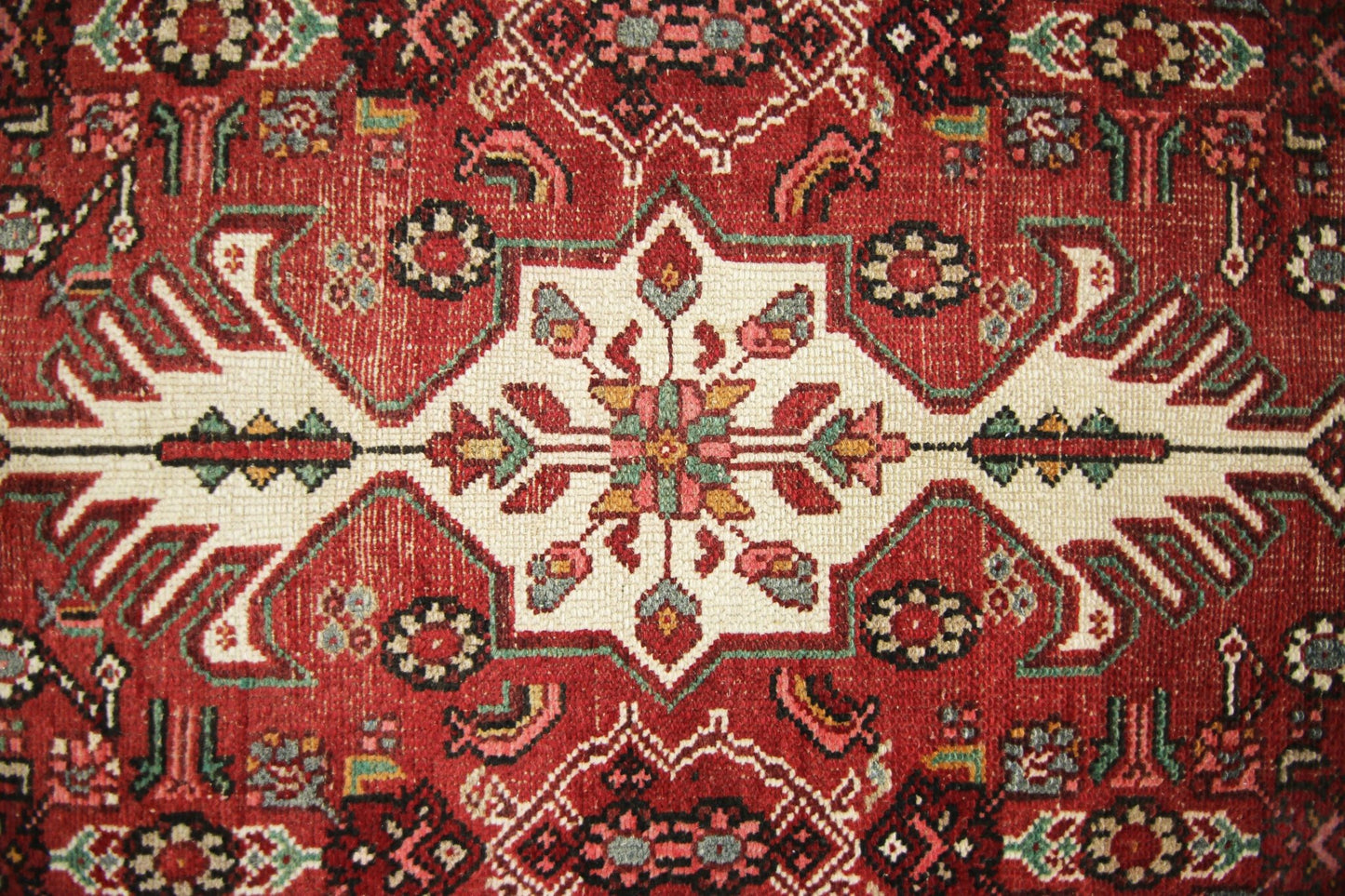 A vintage Persian runner featuring a geometric floral medallion pattern in red, cream, and green.
