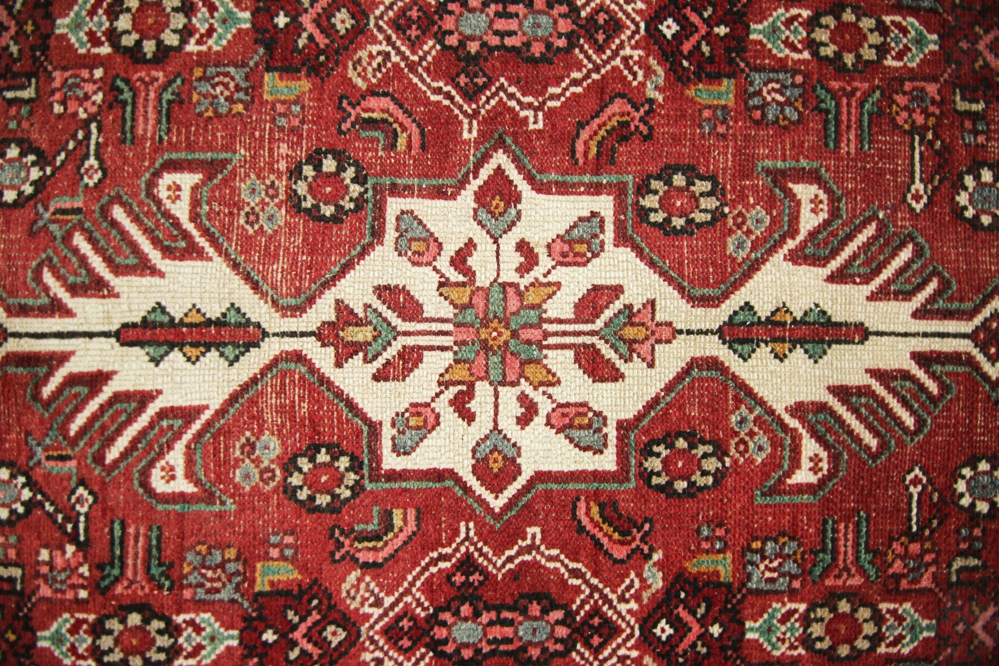 A vintage Persian runner featuring a geometric floral medallion pattern in red, cream, and green.