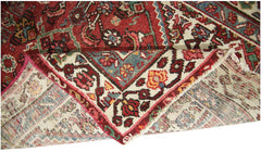 A corner of a vintage Persian runner with a red field and intricate floral patterns.