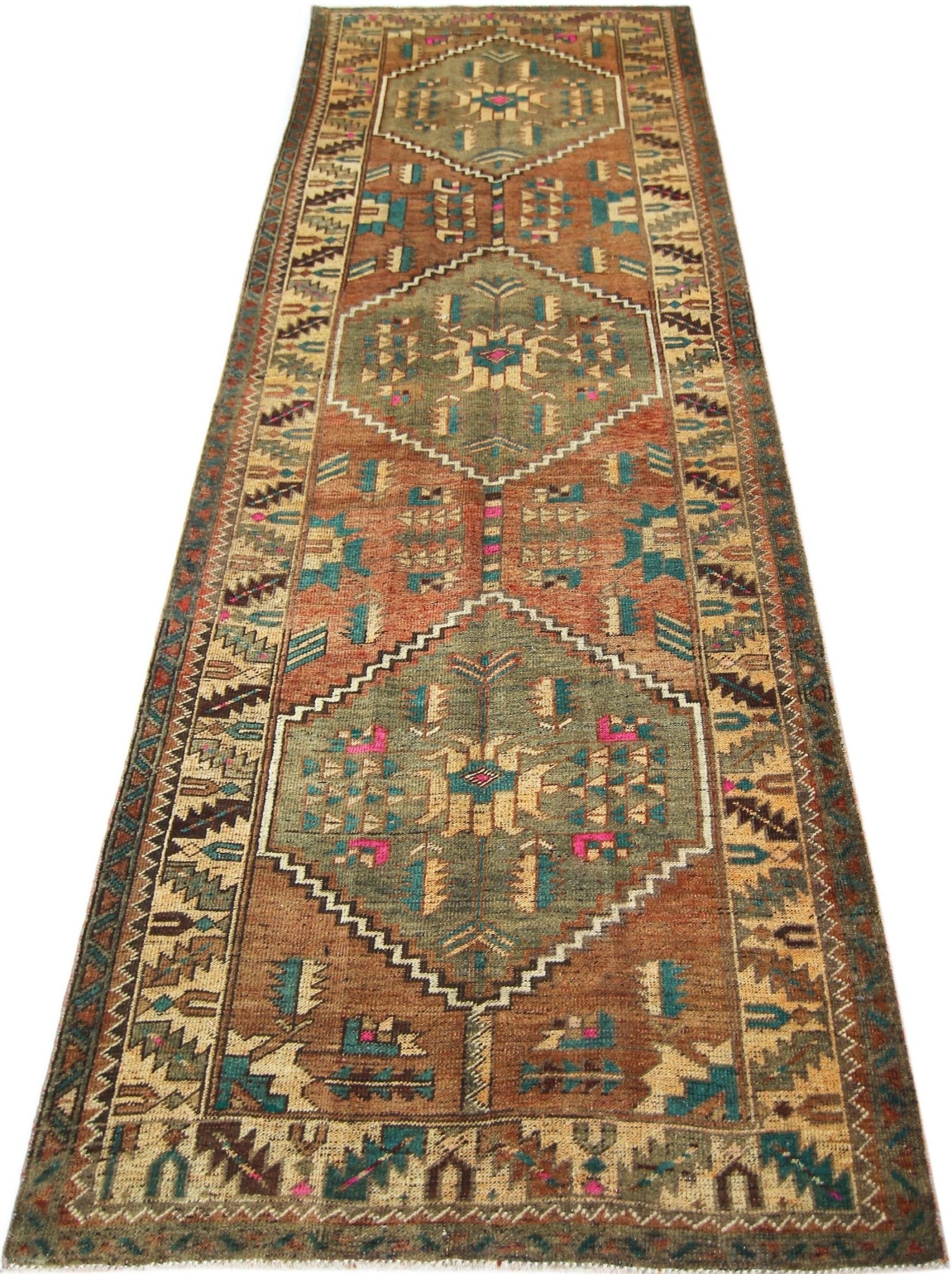 A vintage handmade Persian runner rug featuring geometric diamond medallions in earthy tones.