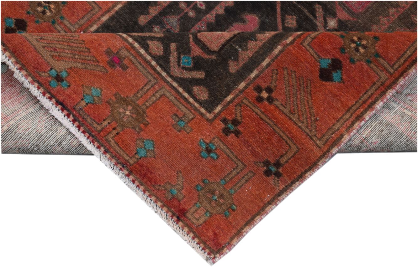 A corner view of a handmade vintage Persian runner featuring geometric patterns in red and black.