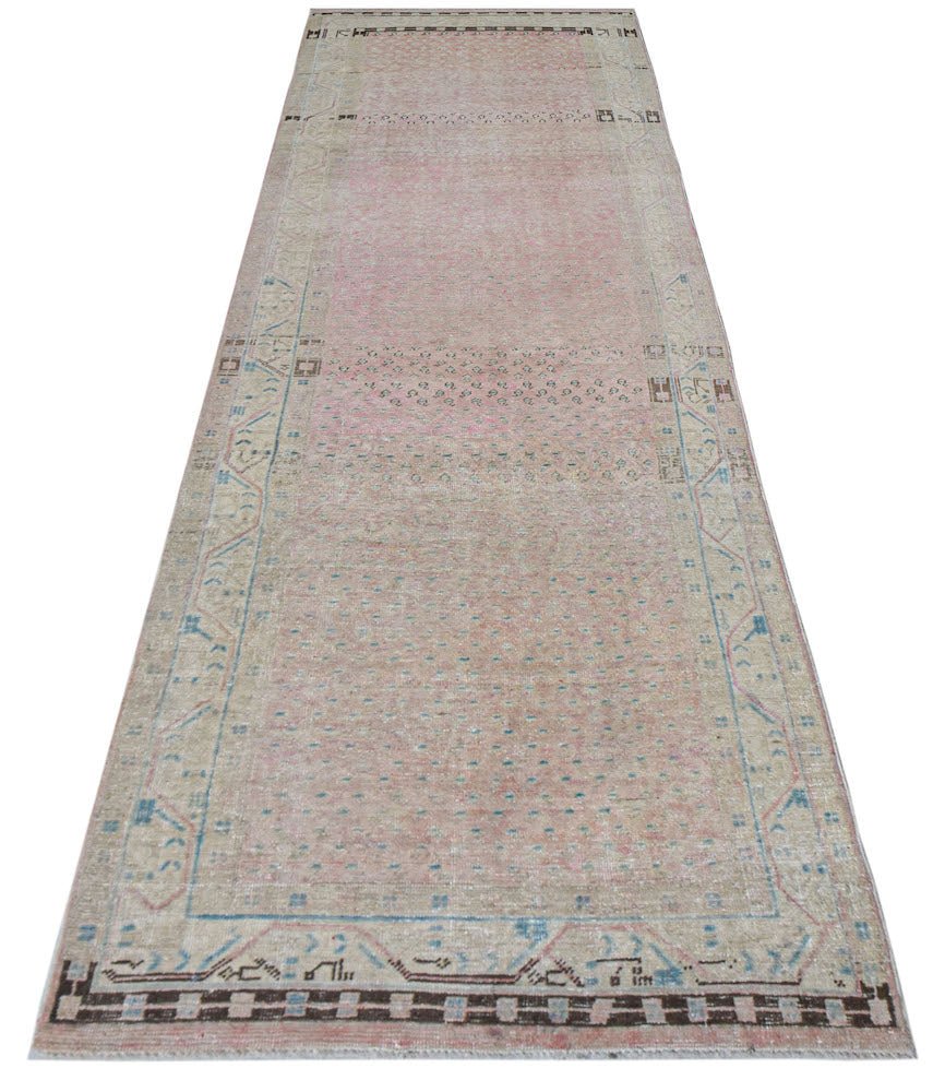 A vintage handwoven Persian runner rug featuring a faded pink field with blue and beige accents.