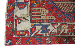 A corner detail of a vintage Persian runner featuring geometric patterns in red, blue, and cream.