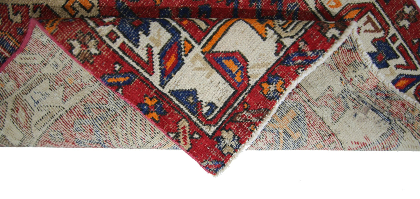 A folded vintage Persian runner featuring a geometric pattern in red, blue, and cream wool.