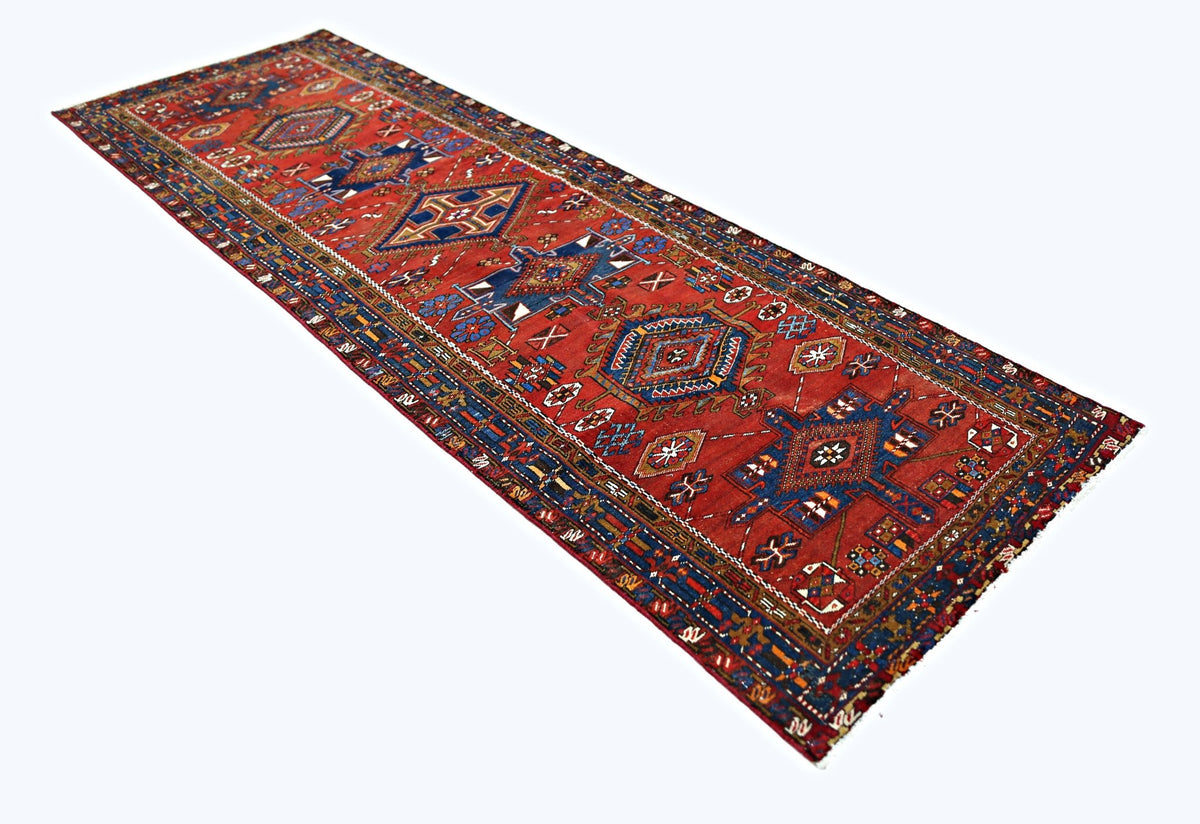 A vintage Persian runner rug featuring geometric medallions in red, blue, and cream tones.
