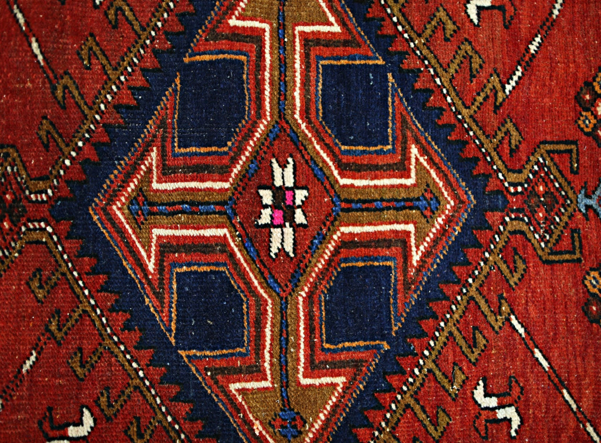 A vintage Persian runner featuring a geometric diamond medallion in red, blue, and brown wool.