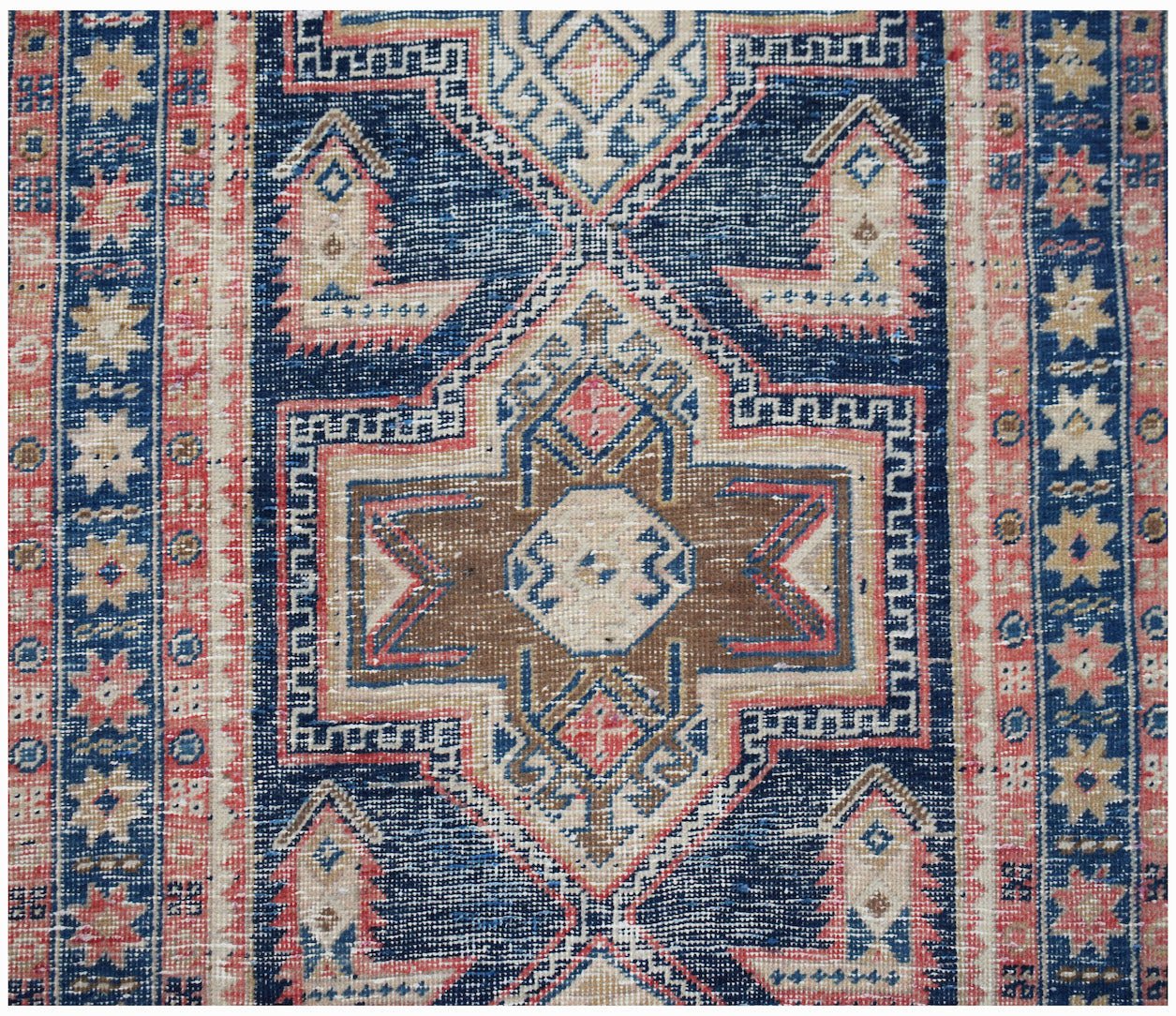 A vintage handwoven Persian runner featuring a geometric medallion pattern in blue, brown, and pink.