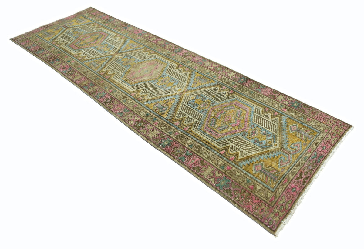A vintage Persian runner rug featuring geometric patterns in shades of pink, blue, and gold.