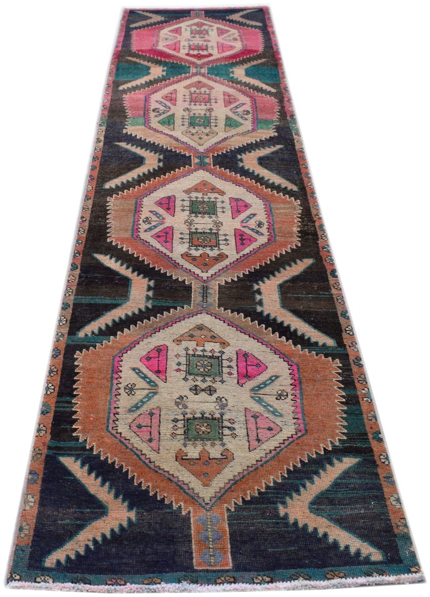 A handmade vintage Persian runner rug featuring geometric diamond motifs in pink, orange, and blue.