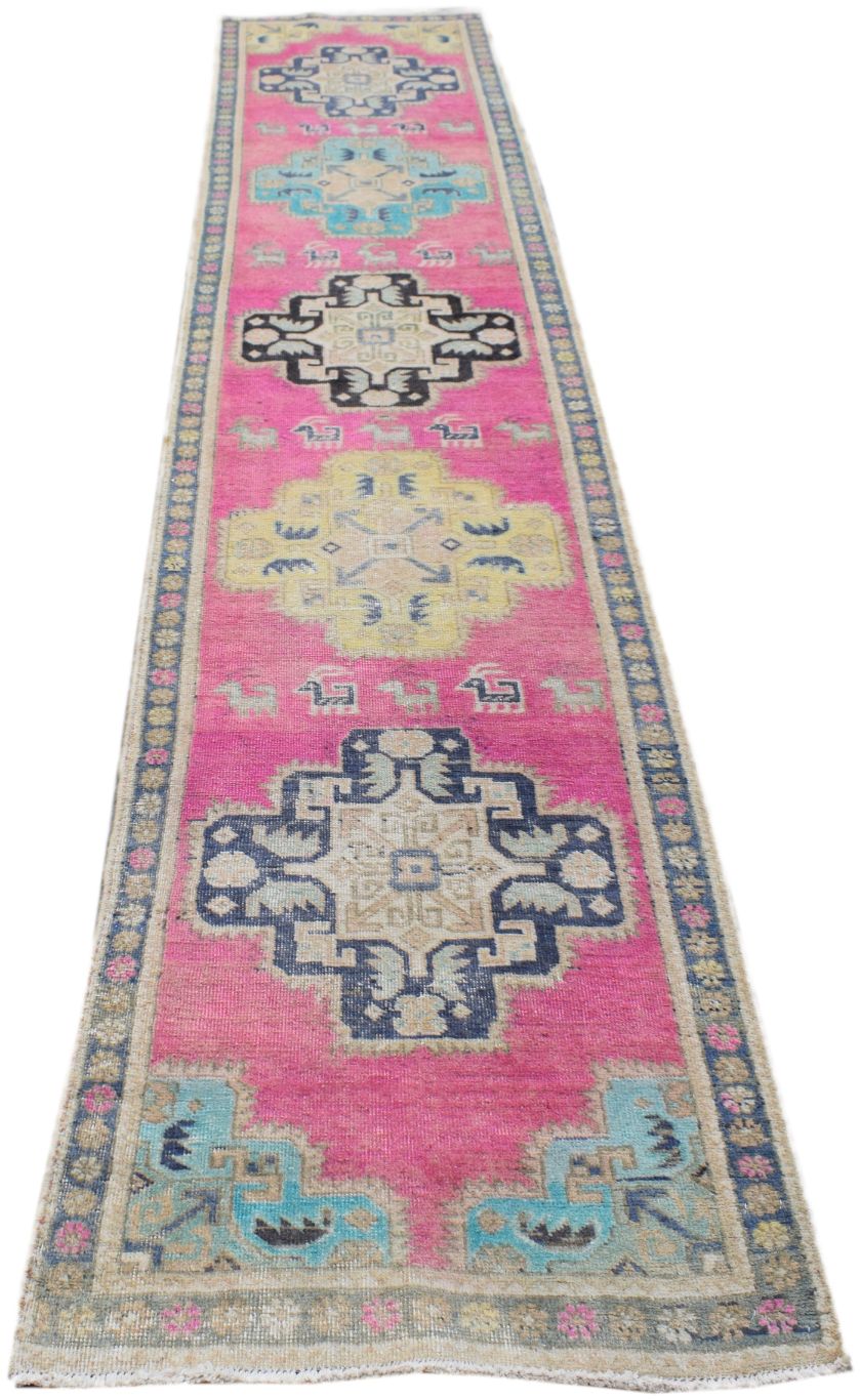 A handmade vintage Persian runner rug featuring geometric medallions on a vibrant pink background.