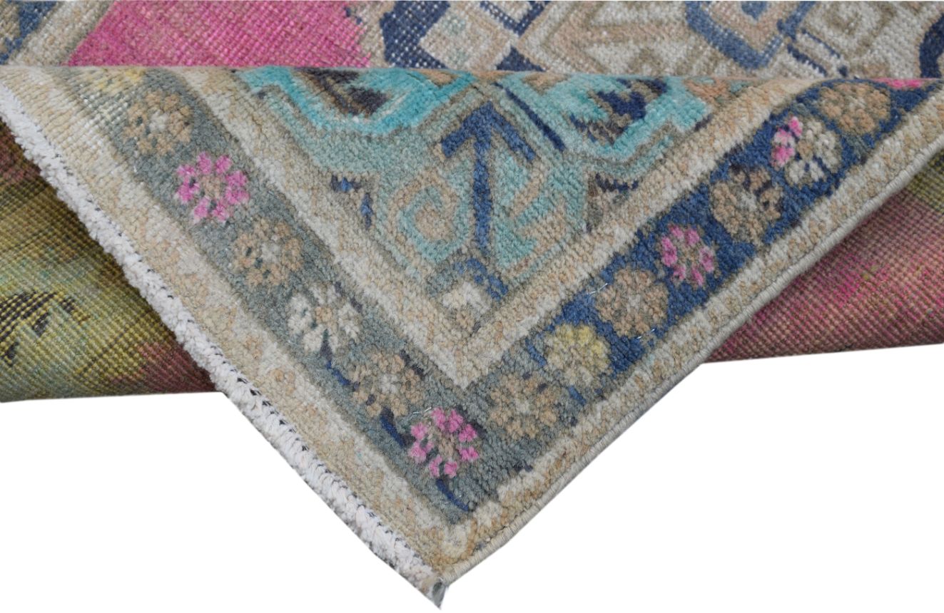 A corner of a handmade vintage Persian runner featuring a floral pattern in blue, pink, and tan.
