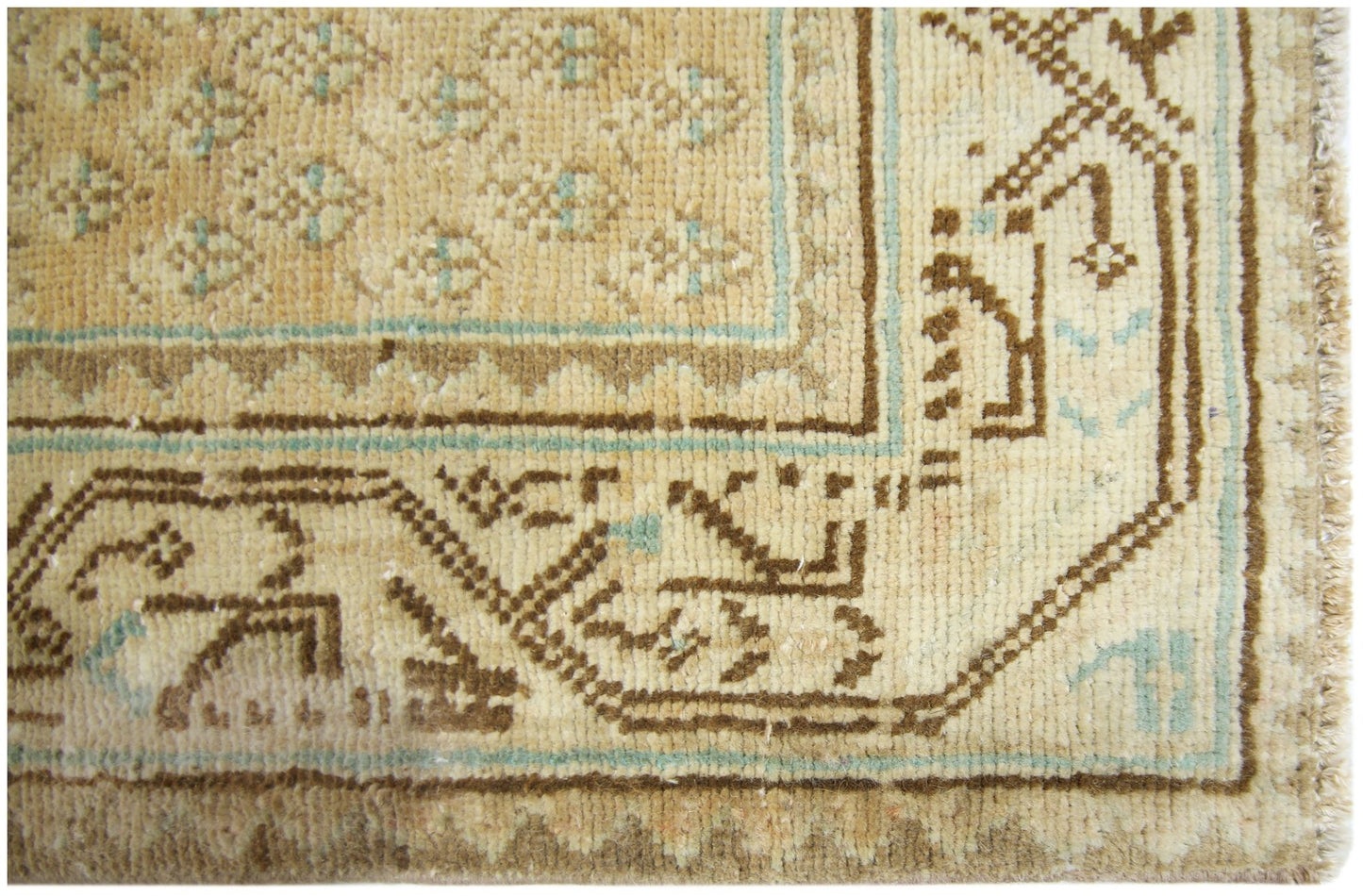 A close-up of a vintage Persian runner featuring geometric brown and teal patterns on a tan field.