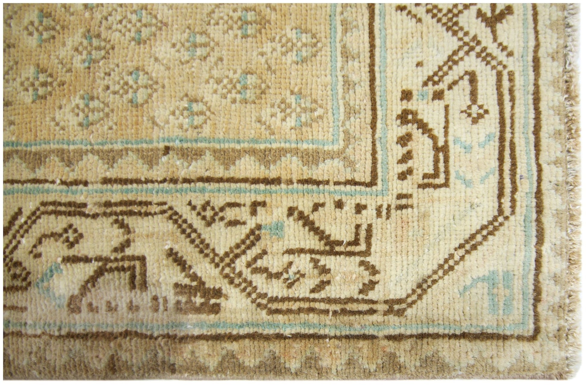 A close-up of a vintage Persian runner featuring geometric brown and teal patterns on a tan field.