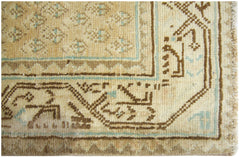 A close-up of a vintage Persian runner featuring geometric brown and teal patterns on a tan field.