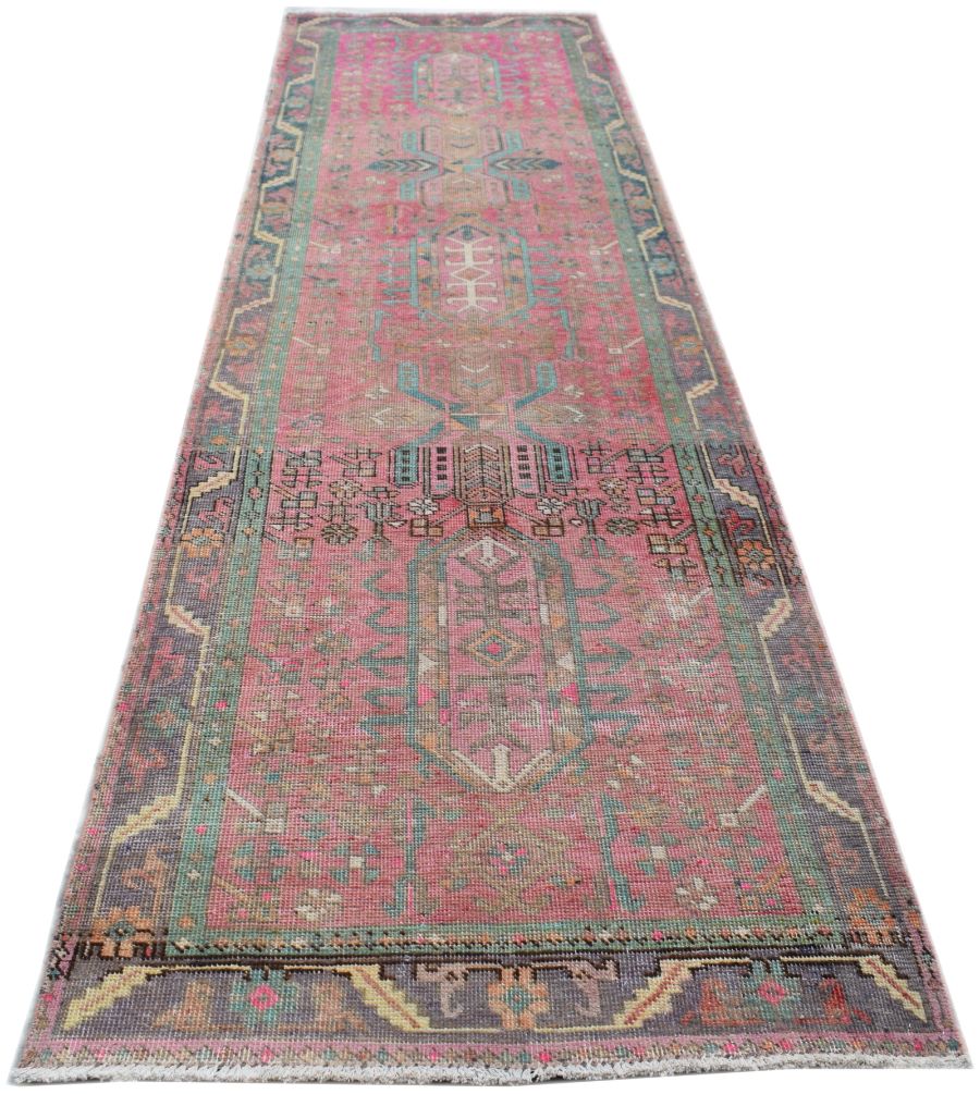 A vintage handmade Persian runner rug featuring a vibrant pink field with intricate tribal patterns.