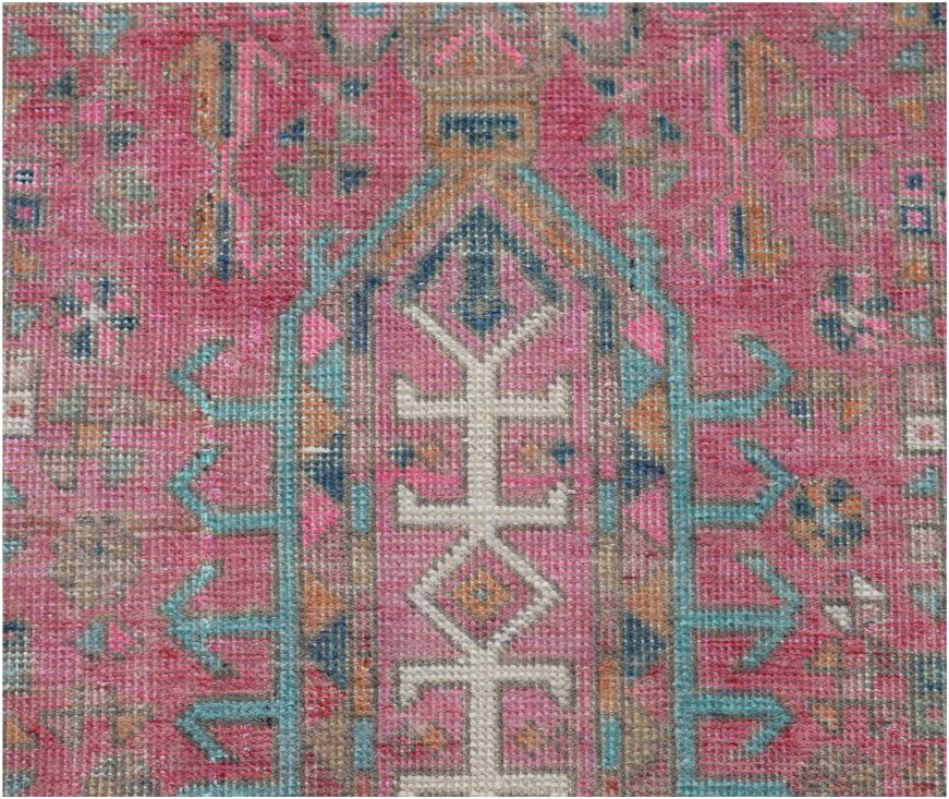 A vintage Persian runner featuring a central geometric motif in pink, blue, and cream wool.